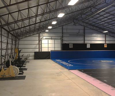 The inside of a recreational metal building with exercise bikes and a wrestling mat