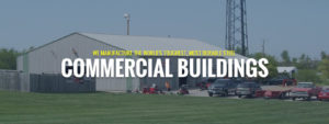 A large commercial building with a metal exterior is surrounded by vehicles and equipment on a grassy area. The text reads, "We manufacture the world's toughest, most durable agricultural steel buildings.