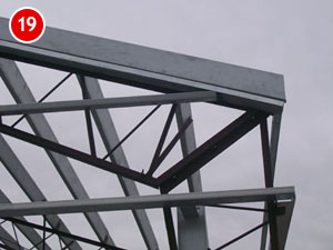 Steel building construction framework with beams against a gray sky. A red circular label with the number 19 is in the corner.