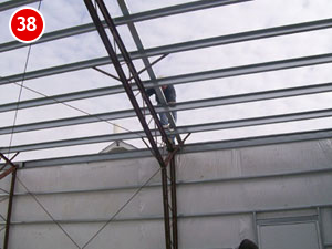 A person is diligently working on the metal framework of a steel building roof under a cloudy sky. The structure, supported by beams, seems to be part of a building under construction. A red circle with the number 38 is in the top left corner of the image.
