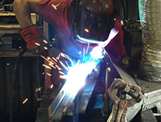 In an industrial workshop, a skilled craftsman wearing protective gear welds metal, with bright sparks dancing around. This focused display of craftsmanship highlights the safety precautions taken in creating high-quality Worldwide Steel Buildings.