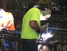 An action shot of a Worldwide Steel Buildings' employee welding steel to make trusses for their custom steel building kits.