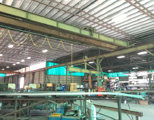The interior of this spacious steel building features industrial equipment, including a large crane. Shelves filled with various materials and boxes line the walls. Bright lighting and exposed metal beams are visible in the ceiling, exemplifying the craftsmanship of a top steel building manufacturer.