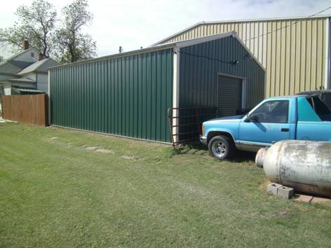 A dark green, steel, outdoor garage designed and built by Worldwide Steel Buildings for a client in Kansas.