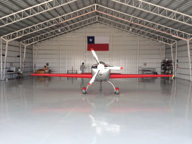 An interior shot of a steel airplane hangar with a plane parked and a Chilean flag hung up.