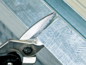 A pair of tin snips being used to cut a sheet of metal