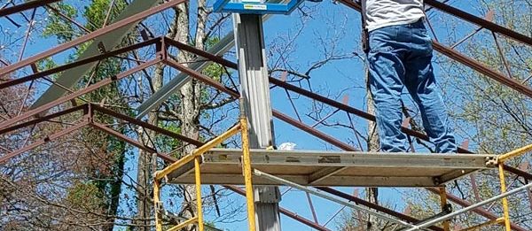 An employee of Worldwide Steel Buildings putting together the steel structure of a new outdoor garage.