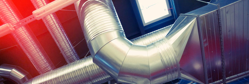 A modern indoor ventilation system with a network of shiny metal ducts casts a soft red light on the left. An AC unit hums quietly, helping to beat the heat, while a rectangular window in the background allows natural light to enter.