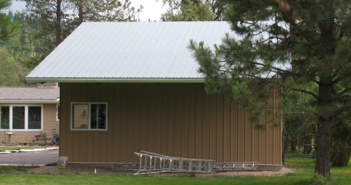 View from the side of a custom metal garage with a garage overhang built by Worldwide Steel Buildings.