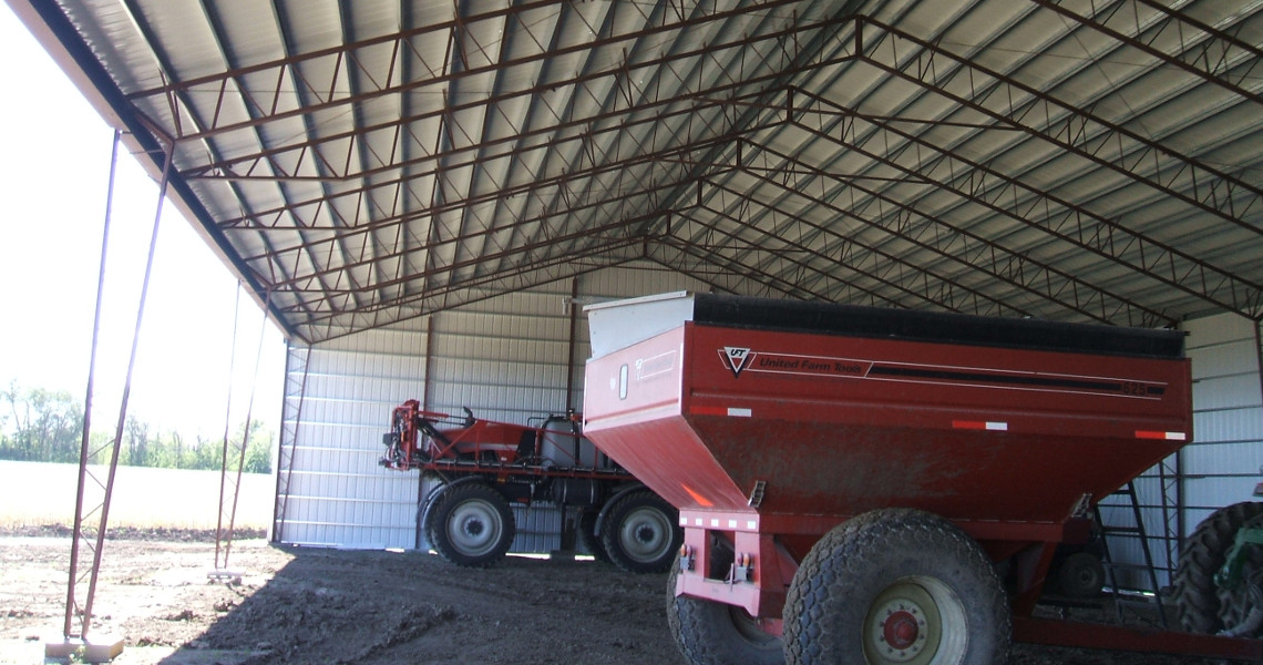 An equipment storage building designed and built by Worldwide Steel Buildings with two pieces of farming equipment inside.