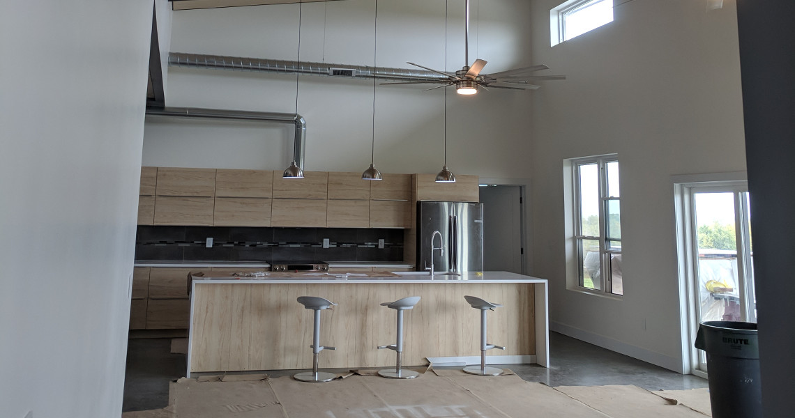 A shot of the entire kitchen inside of a metal barndominium featuring light wood and stainless steel appliances.