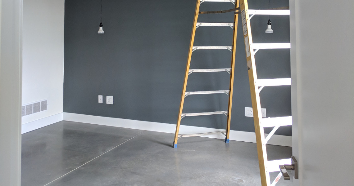 A step ladder inside of a room with light gray tile flooring and dark gray walls.