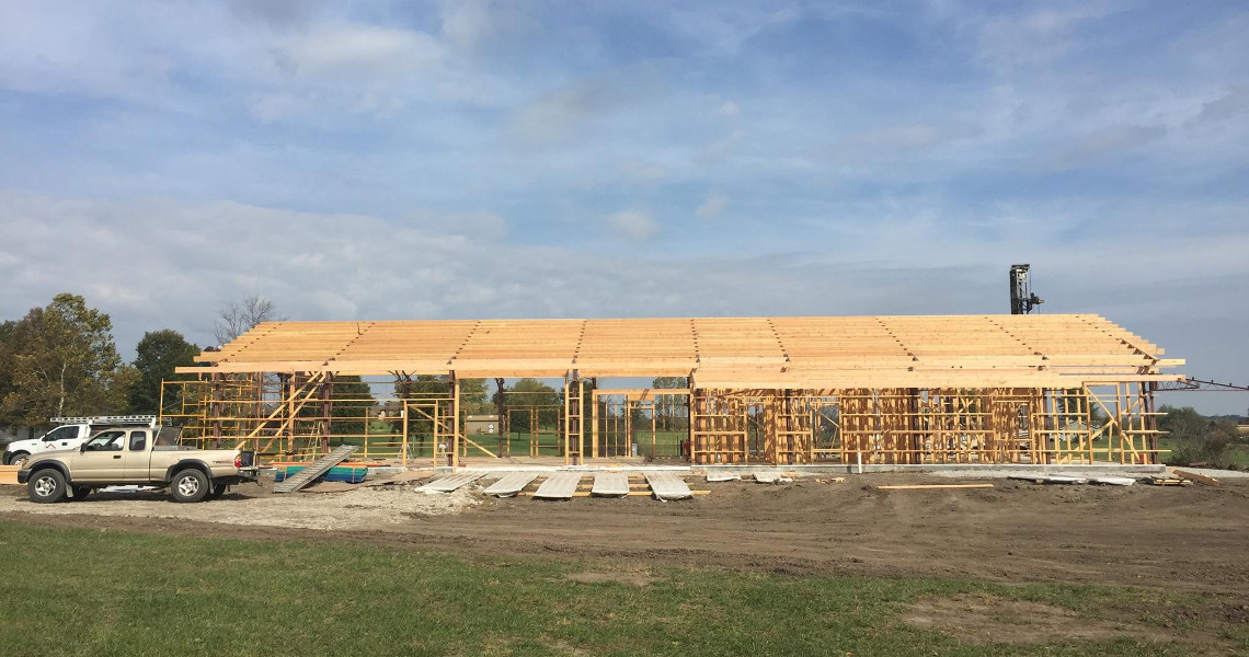 A construction site showcases a partially built wooden structure, with a sturdy framework and roof in progress. The white truck parked on the grassy area hints at the future completion of this Duncan dream home, all under a cloudy sky.