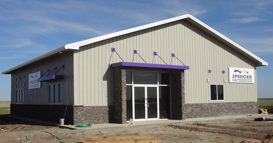 A newly constructed building with gray siding and stone accents boasts large windows and purple awnings. The signage reads 