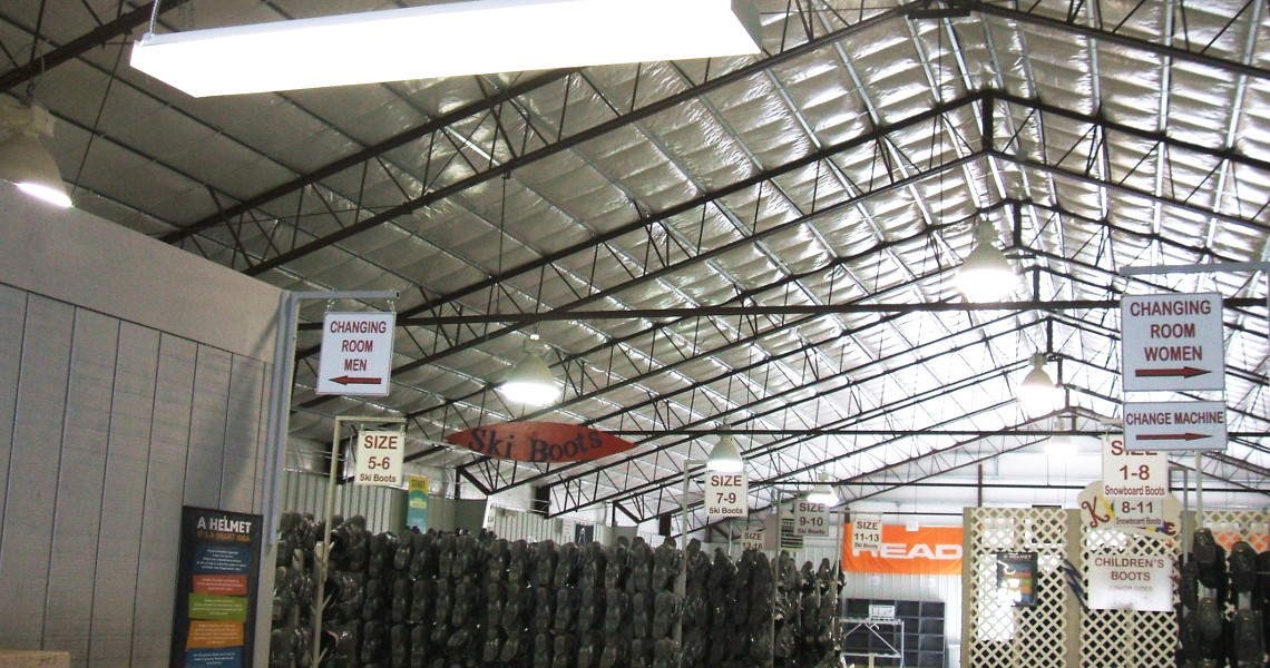 The interior of Snow Creek Ski Resort's rental shop features a high, metal-framed ceiling. Signs for men's and women's changing rooms and ski boot sizes are visible, while rows of neatly lined ski boots await eager skiers.