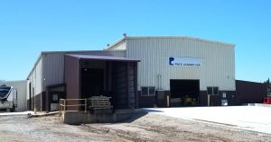 The exterior view showcases a large industrial building labeled "Pack Leader USA," featuring light-colored metal and a brown loading dock area. This impressive storage facility stands against a backdrop of clear blue skies, with a paved driveway enhancing its robust presence.