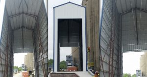 Three images of a large industrial structure under construction at the Bartlett site, showcasing a tall, open-ended building with steel frameworks and white-blue panels. Construction equipment and temporary structures are visible around this future grain facility.