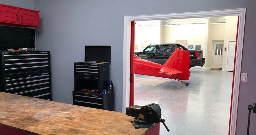 View through an open door of airplane tail and truck parked in hangar.
