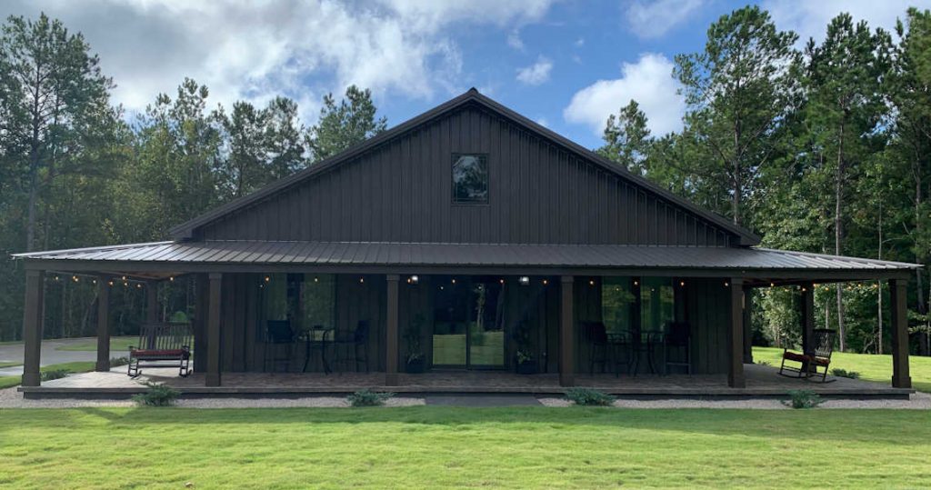 Black ranch-style barndominium with wraparound porch.
