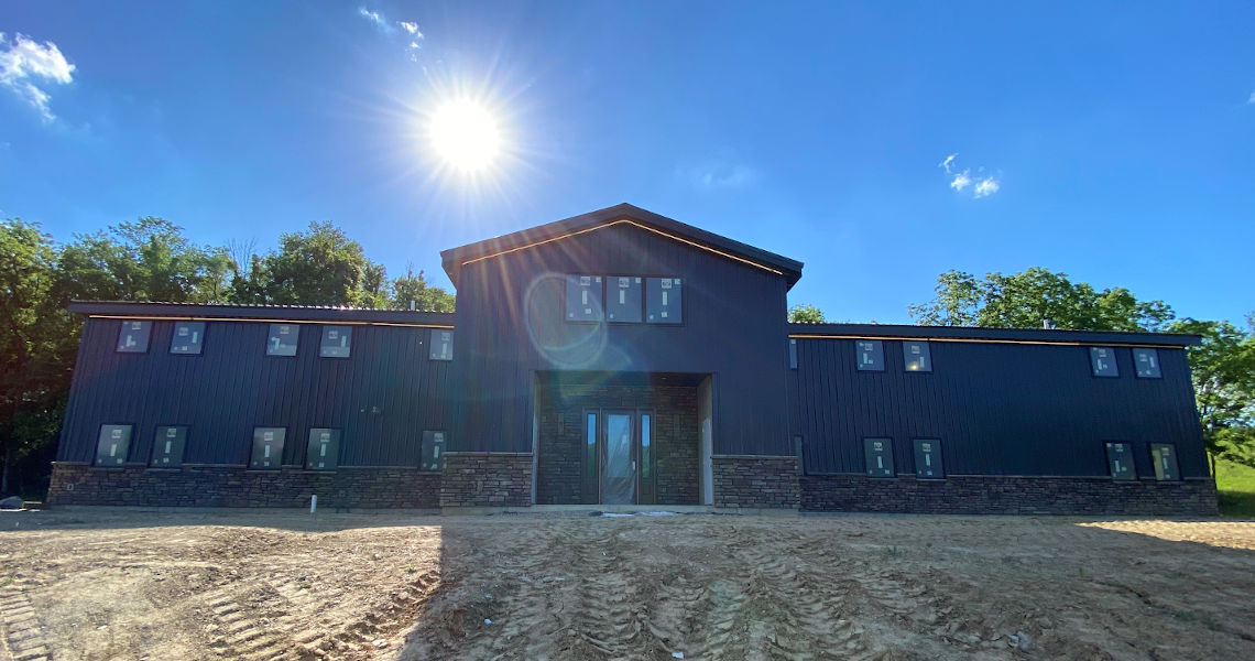 Front of large black barndominium with sun shining over the roof.