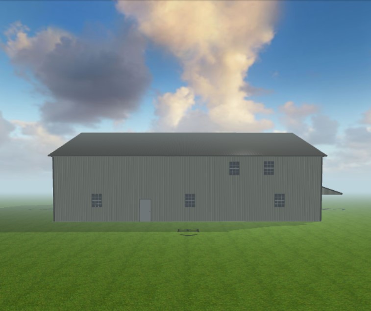 A large, simple building with gray exterior and small windows, standing on a grassy field under a blue sky with scattered clouds. The structure has a single door and appears industrial or utilitarian in design.