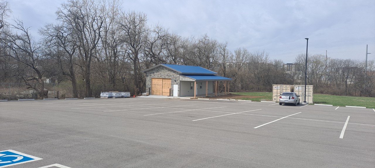 A small, single-story building with a blue roof sits in a mostly empty parking lot. The sign reads 