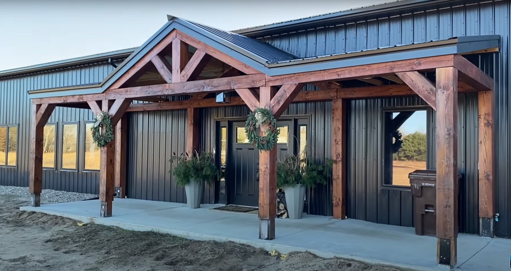 A large, black and beige warehouse with a gabled roof—Ref#013134—features multiple garage doors on one side and a person-sized entrance with two windows adjacent. Set against a cloudy sky, this hybrid structure rests gracefully on a grassy expanse.