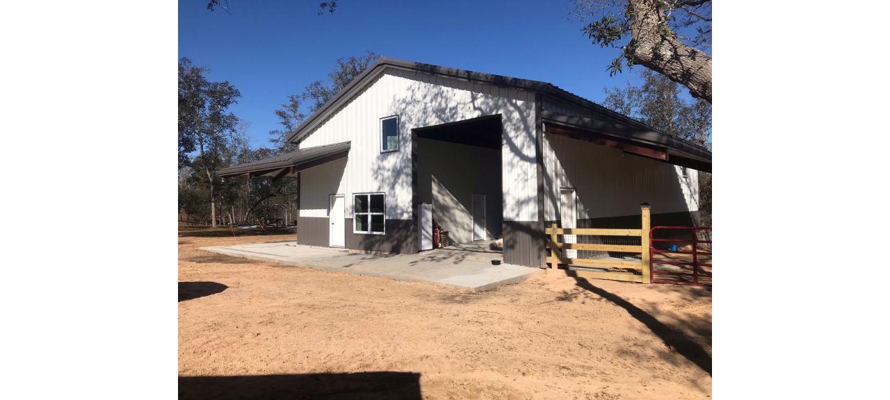 A metal barn with an A-frame roof stands on a dirt lot, marked by the name 