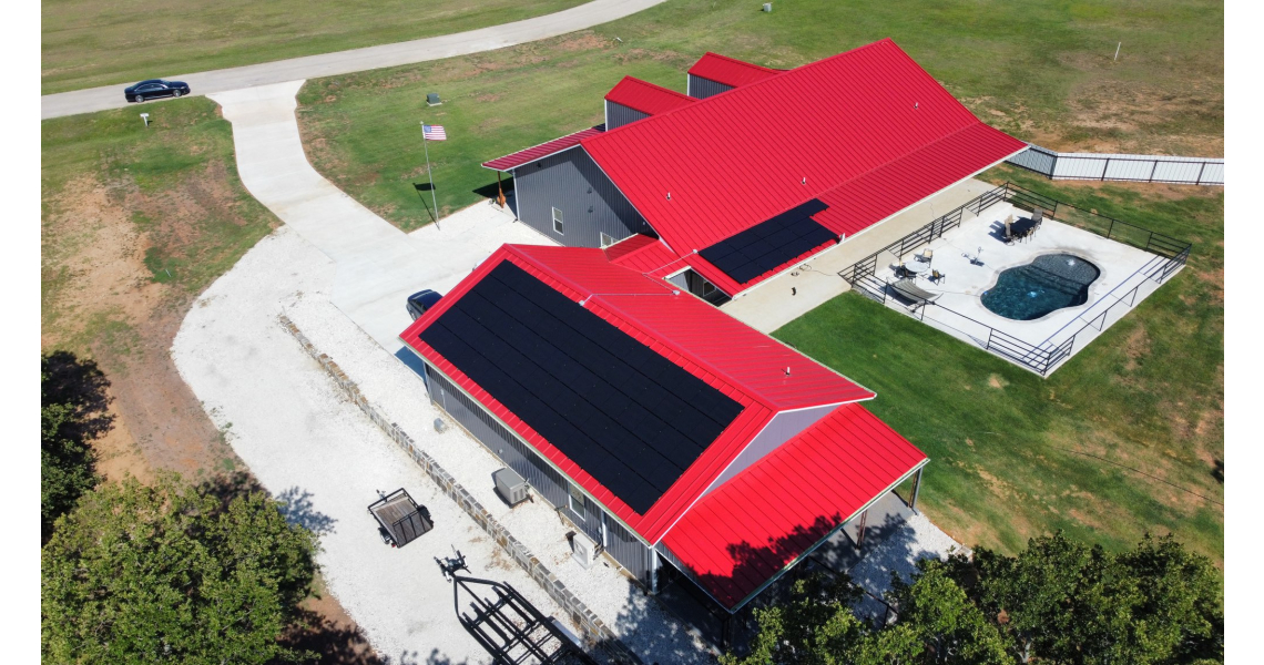 Aerial view of Freeman Residential Home with bright red roofs and solar panels. A paved driveway and parked vehicles are visible. There's a fenced-in outdoor pool and a small grassy area surrounding the house. An American flag is proudly mounted near the driveway.