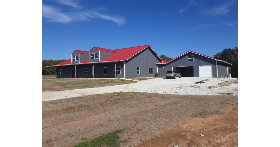 The Freeman Residential Home is a modern gray house with red roofs and white trim, featuring a large garage and driveway. A car is parked near the garage. The sky is clear and blue, complementing the residential home's contrast against the dry, brown lawn.