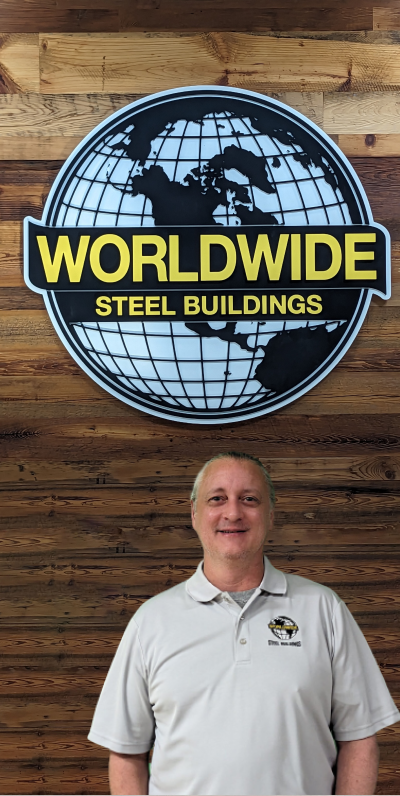 A person with short gray hair wearing a bright blue shirt is smiling at the camera in an indoor setting with beige walls, looking like they're ready to press the builder button.