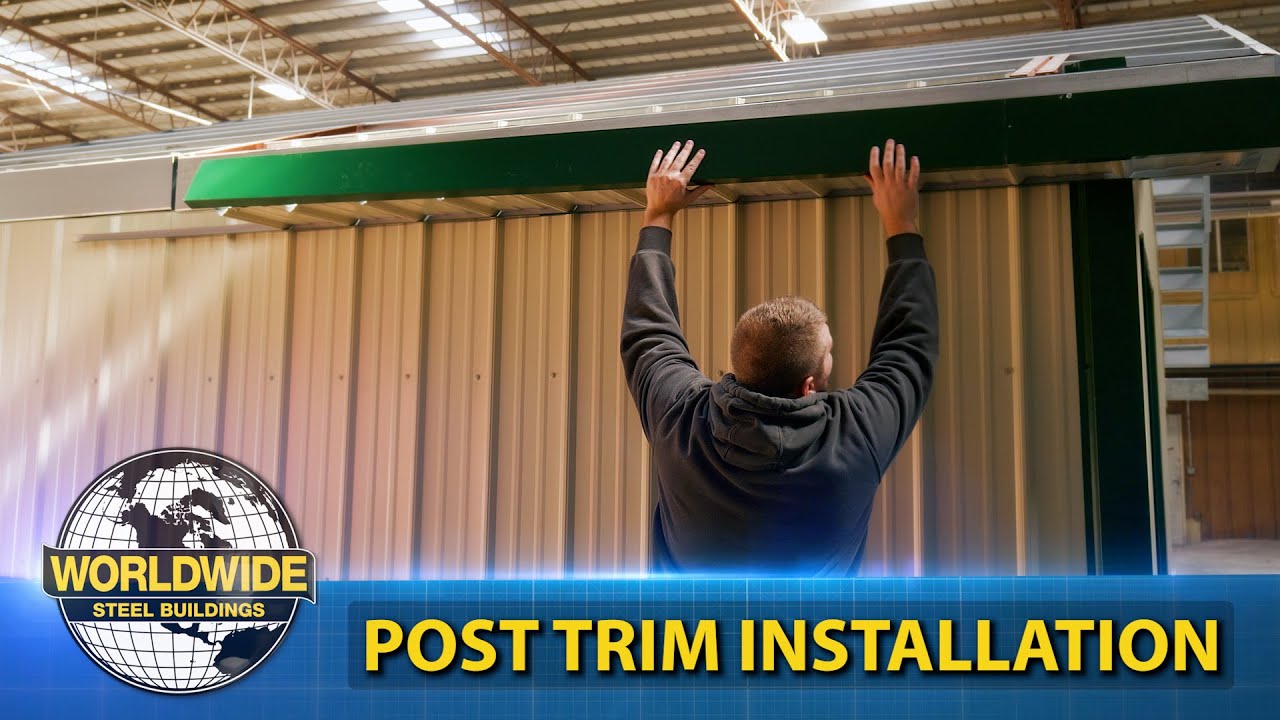 A person installs a trim on a metal building, standing under the eave with arms raised. Text reads "Post Trim Installation" alongside the Worldwide Steel Buildings logo. The setting is inside a large warehouse, showcasing precise installation techniques in action videos.