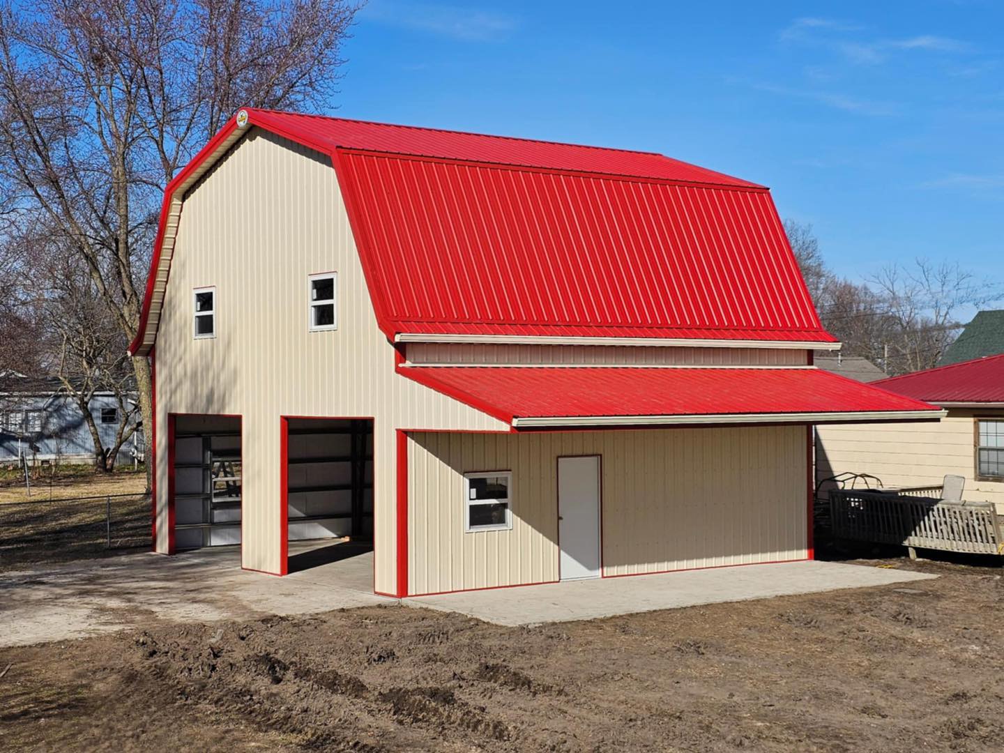 Barn-style building with gambrel roof, garage and regular doors, on concrete foundation under blue sky.