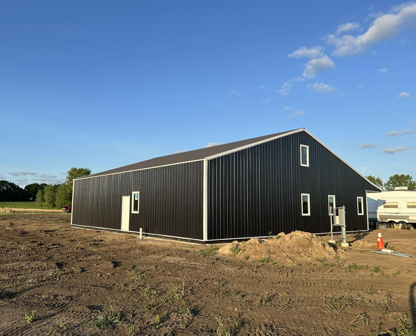 Barndominium with sloped roof on dirt lot under blue sky; windows and door visible, sparse grass around.