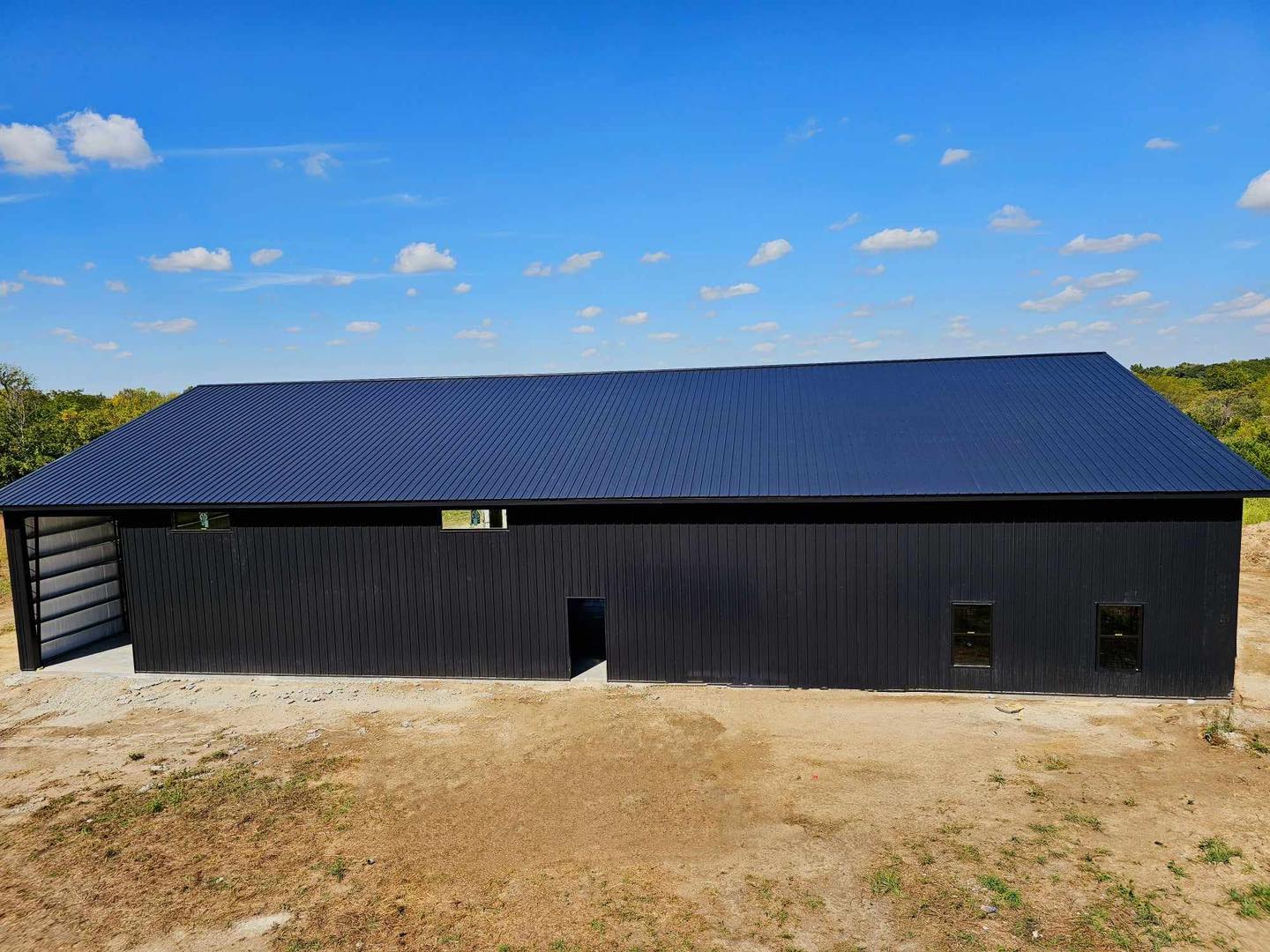 Sleek black structure with blue roof, small windows, and door, set in a tree-lined dirt clearing.