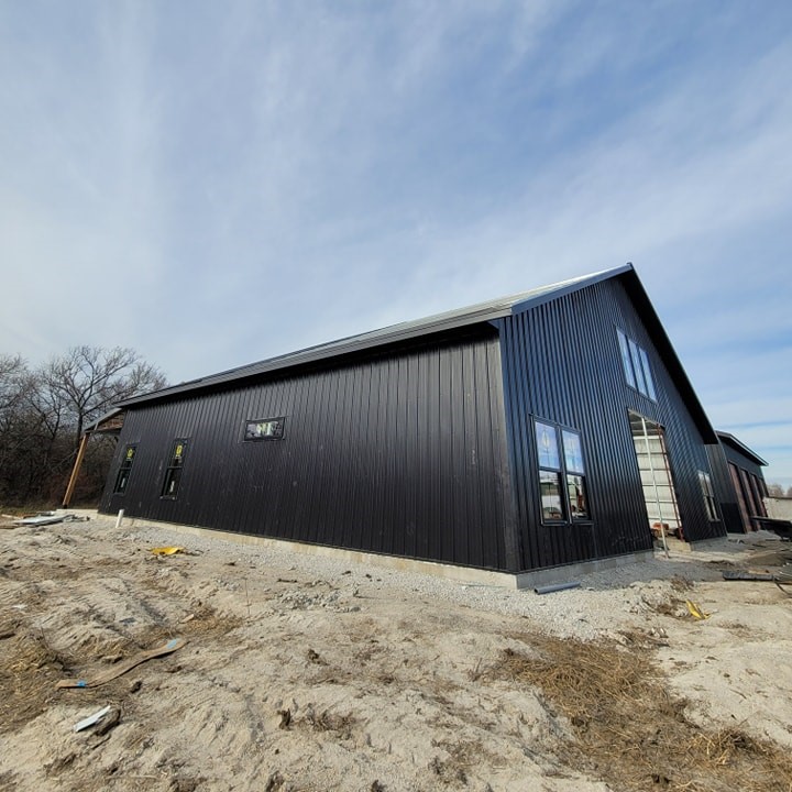 Modern black building with a slanted roof, gravel area, windows, wooden elements, sparse trees.