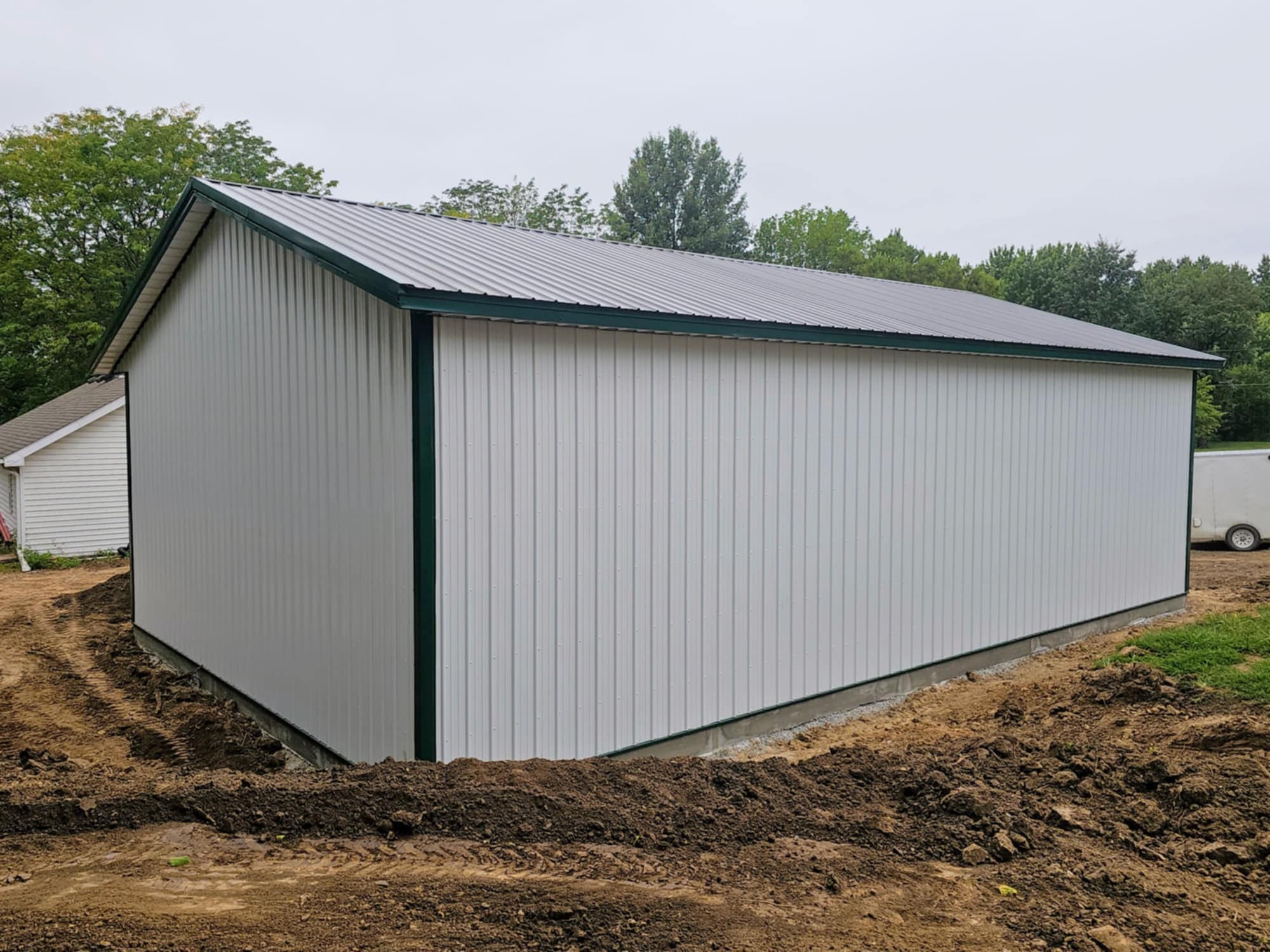 ChapCo's new gray metal shed with dark trim on dirt, trees/buildings in cloudy background.