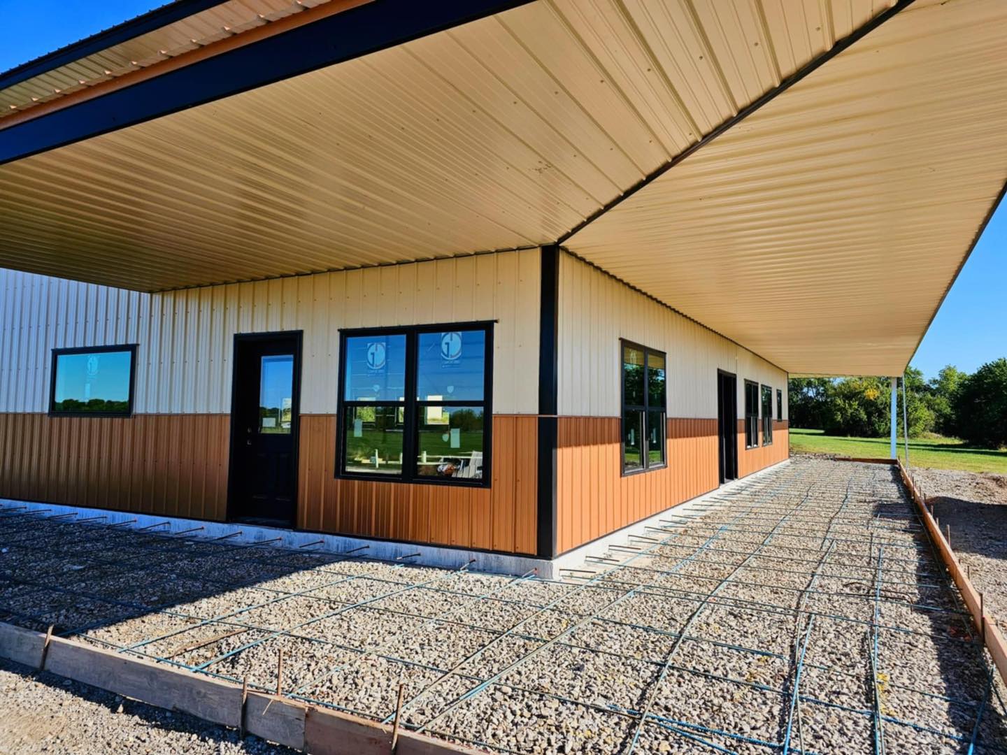 Modern Drexel building with tan/brown siding, flat roof; site prepped for concrete, trees behind.
