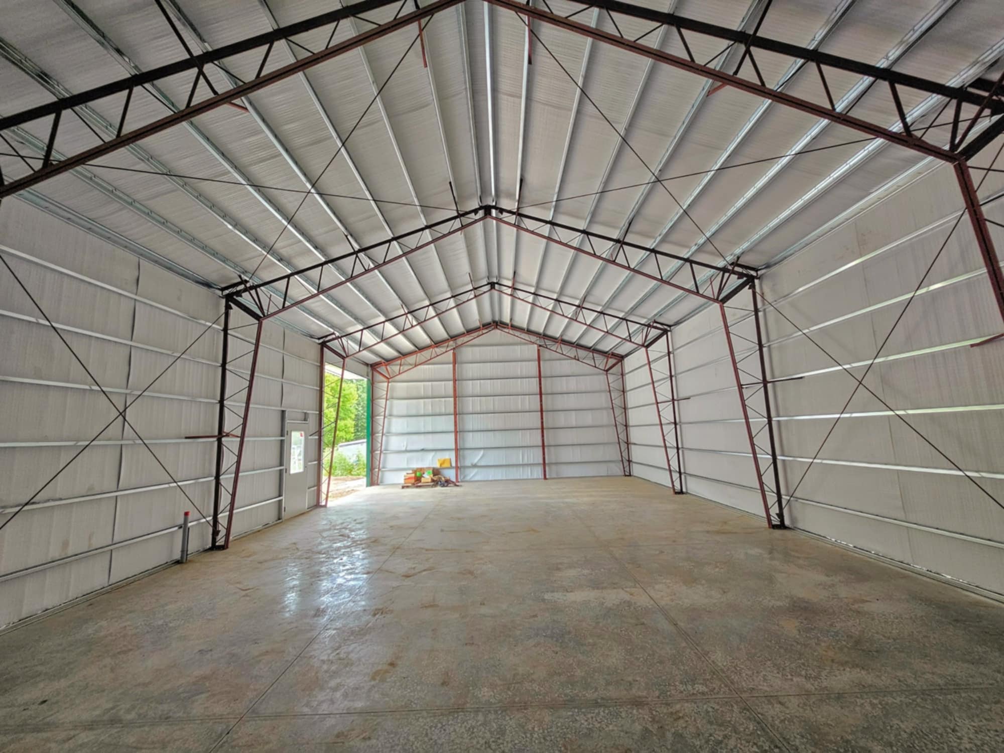 Spacious warehouse with high ceilings, red beams, and sunlight casting shadows on walls and floor.