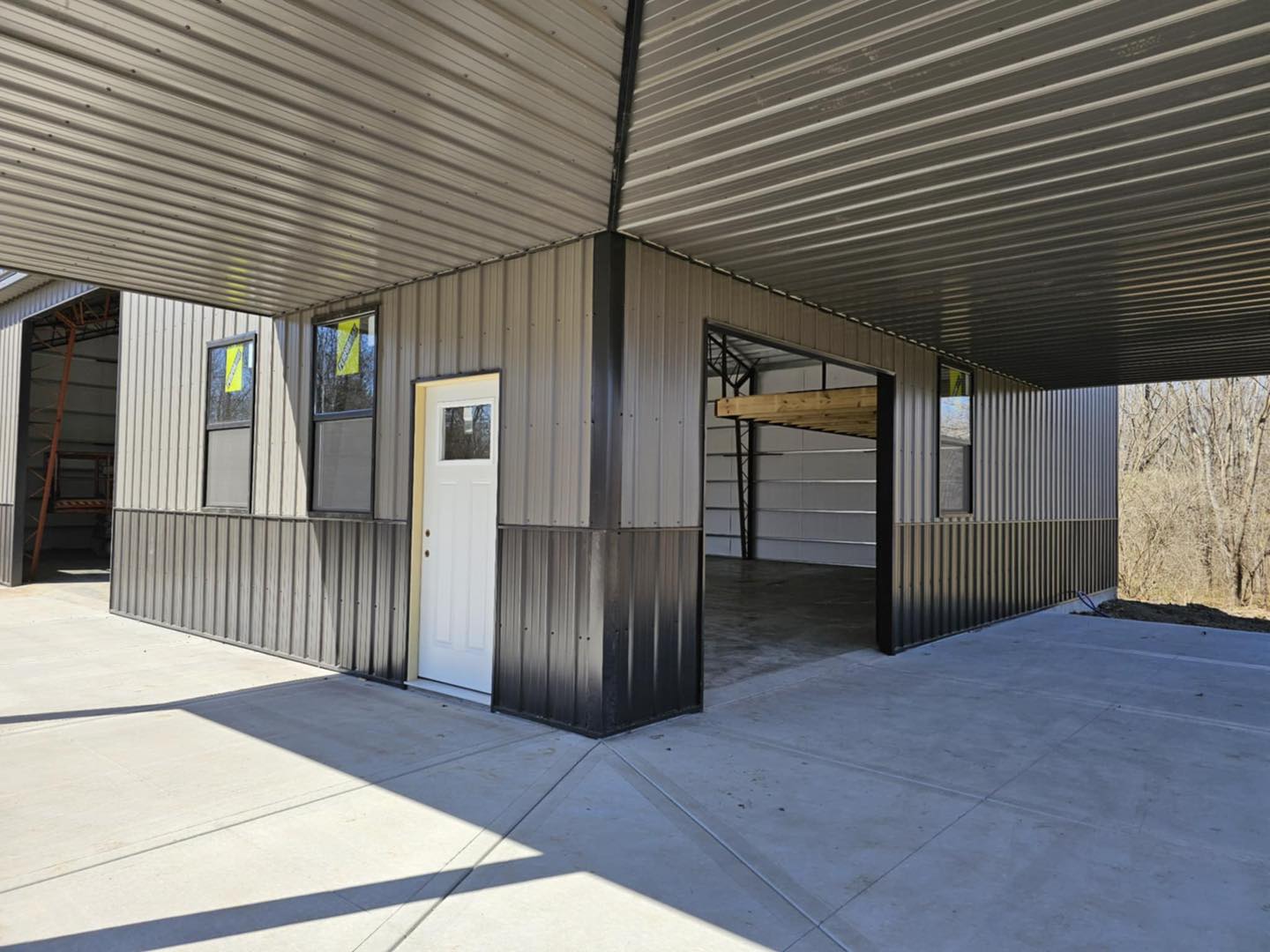 Metal building with open garage, white door, windows; concrete base; trees in the background.
