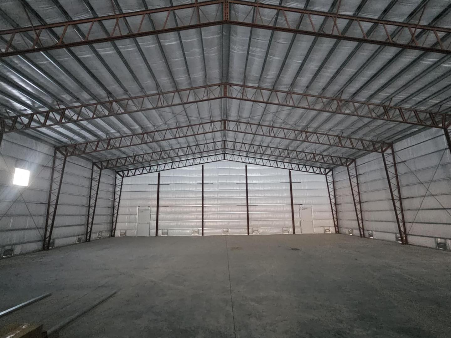 The image depicts the interior of a vast, empty ACCI warehouse. The space features a high, vaulted ceiling supported by exposed metal beams crafted from specialty materials. It is well-lit with natural light streaming through small wall windows, and the floor is a smooth concrete surface.