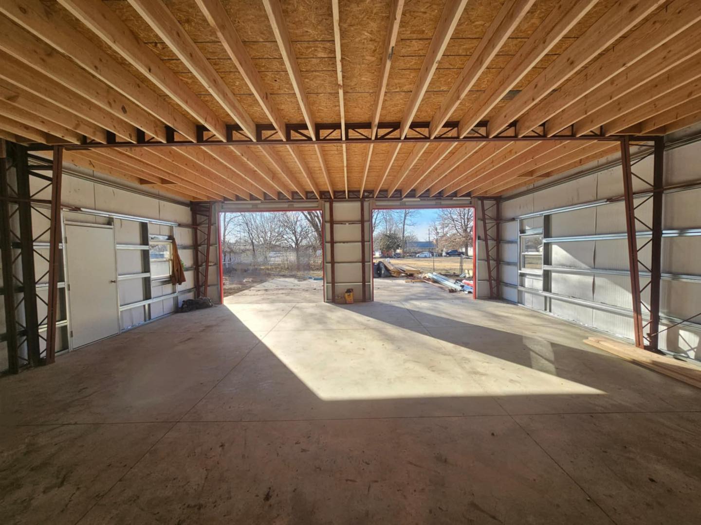 Gambrel garage interior with wooden beams, open door, and views of trees and grass outside. Rustic charm.
