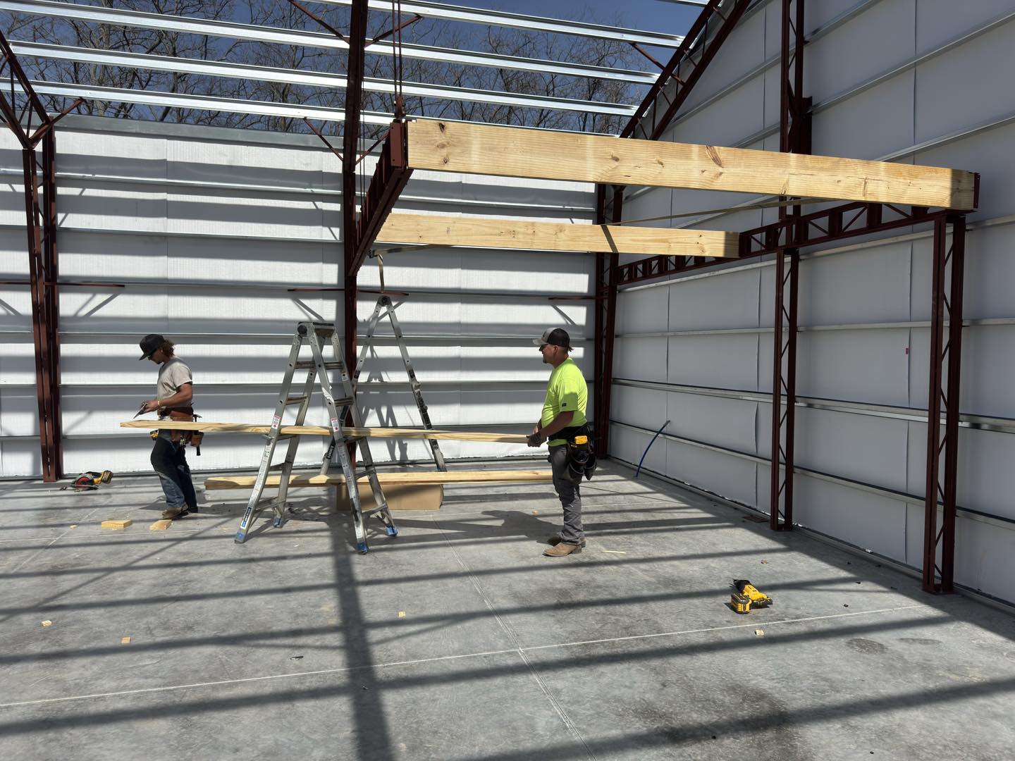 Two workers at Litchford site with a metal frame, tools, ladder, and sunny sky.