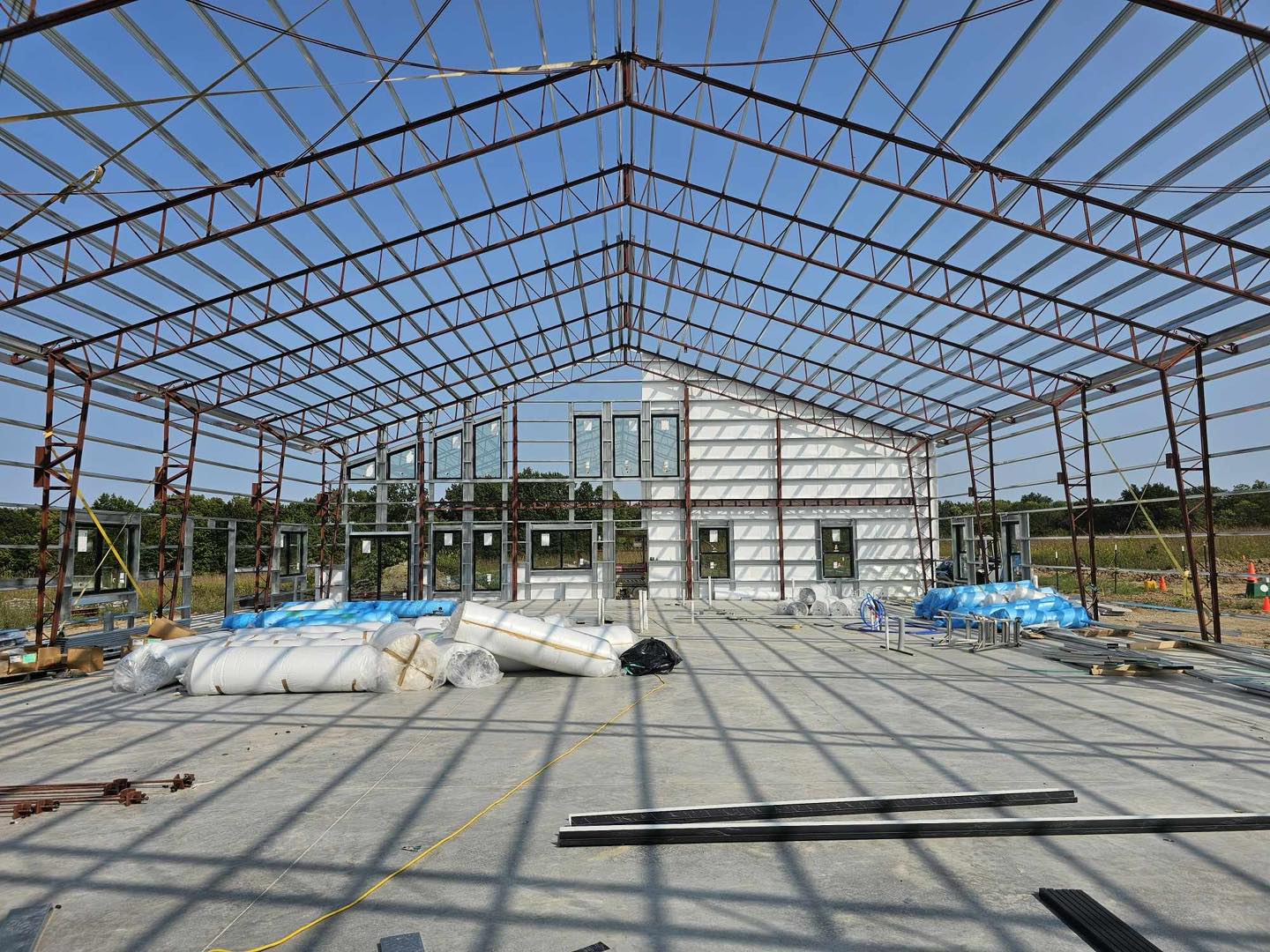 Open construction site with a steel frame barndominium, concrete ground, and scattered insulation material.