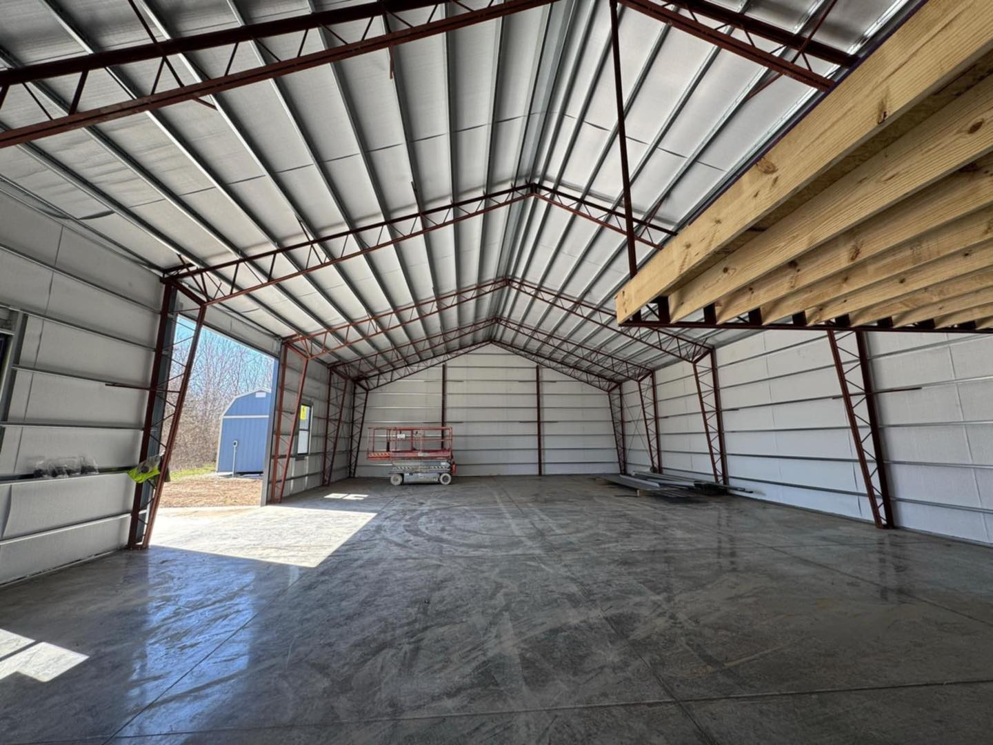 Interior of an empty warehouse with high ceilings, steel beams, and a red scaffold by the entrance.