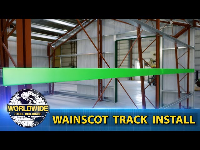 Steel frame with green beam in warehouse; text: "Worldwide Steel Buildings" & "Wainscot Track Install".
