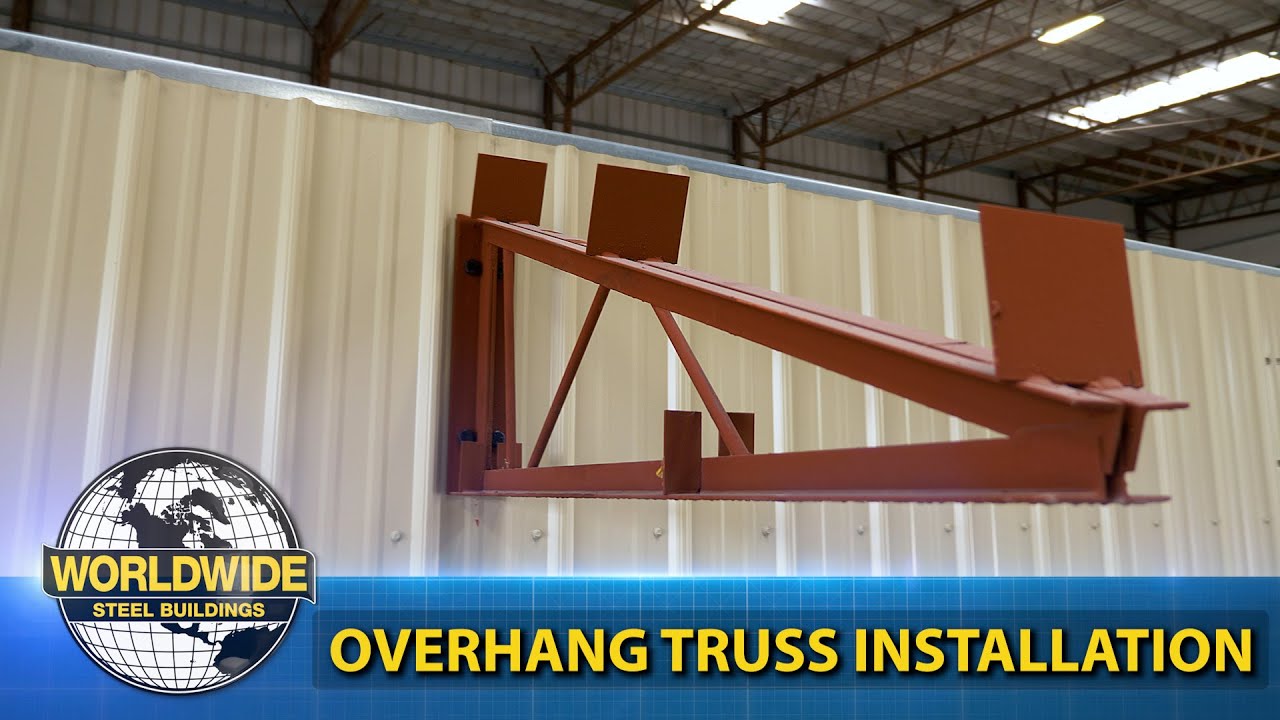 Red steel truss overhang on beige metal building, showing Worldwide Steel Buildings installation.