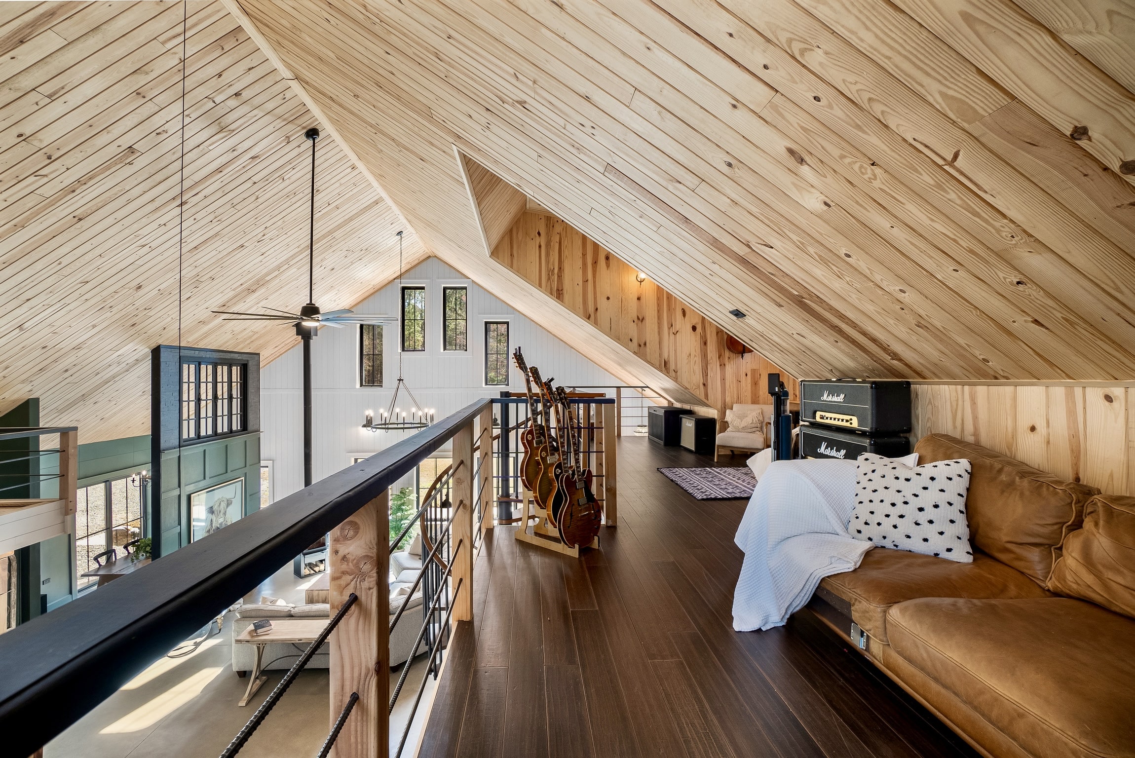 Cozy Shipyard Creek loft with wood walls, brown sofa, guitars, and view of modern living area.