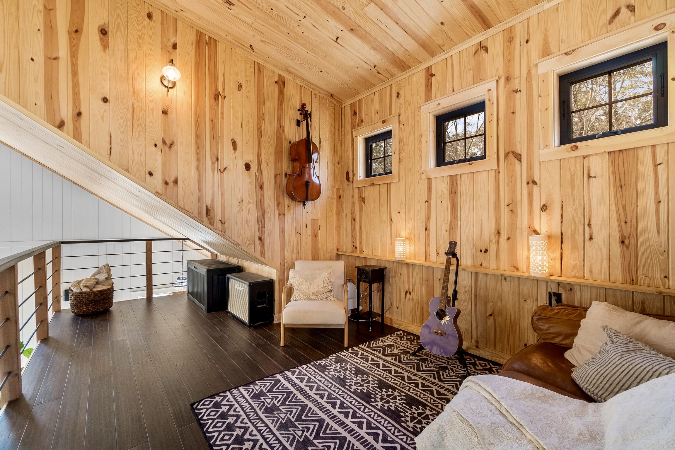 Cozy loft with wood walls, sofa, armchair, instruments, lamps, and dark wood floors.