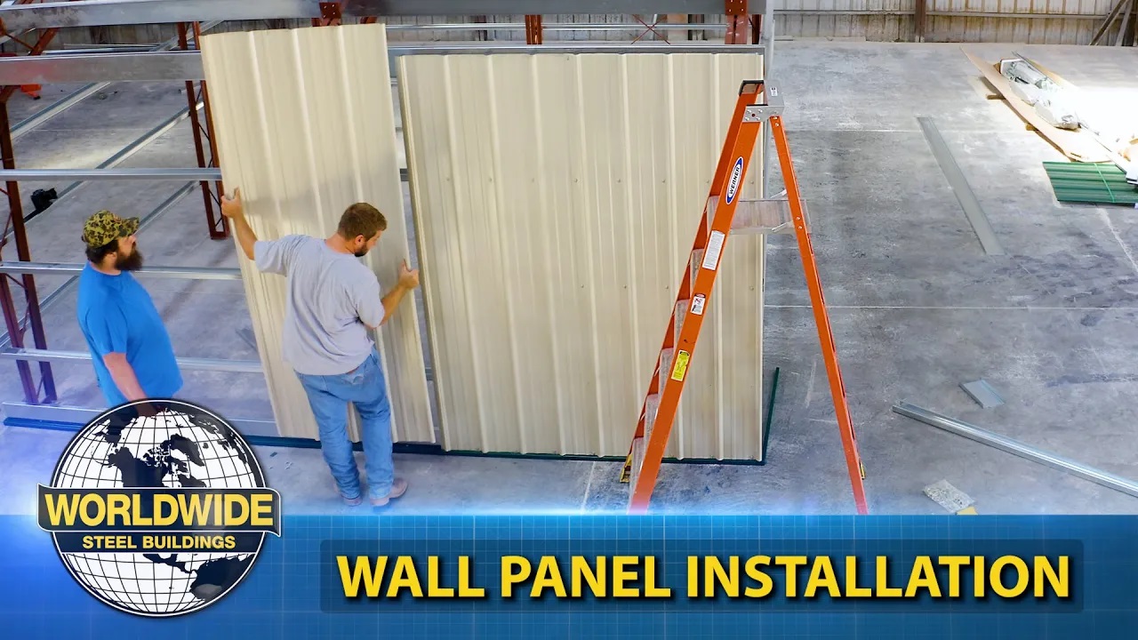 Two men install a metal building indoors with an orange ladder nearby.